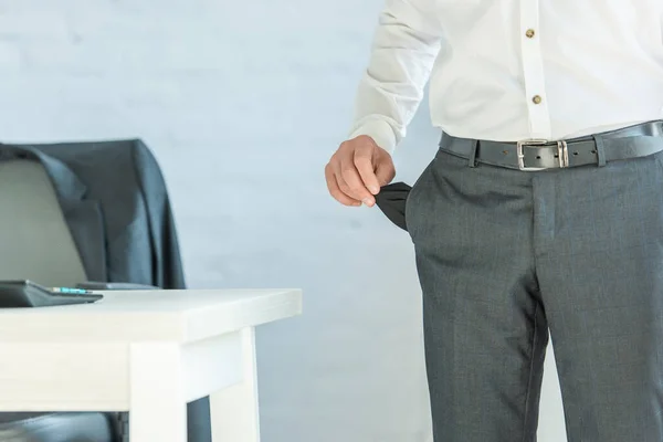 Ausgeschnittene Ansicht eines Bankrotts mit leerer Tasche, während er in der Nähe des Tisches auf verschwommenem Hintergrund steht — Stockfoto