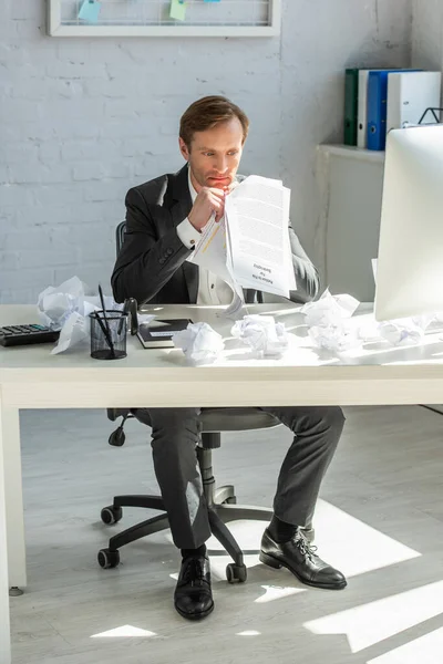 Empresario molesto llevando a cabo una petición de bancarrota, mientras se sienta a la mesa con papeles arrugados en el cargo - foto de stock