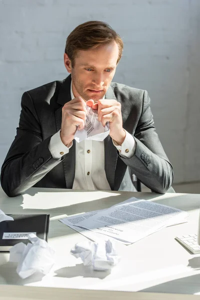 Depressiver Geschäftsmann sitzt mit zerknittertem Papier am Arbeitsplatz in der Nähe des Insolvenzantrags — Stockfoto