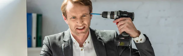 Angry businessman holding drill near temple on blurred background, banner — Stock Photo