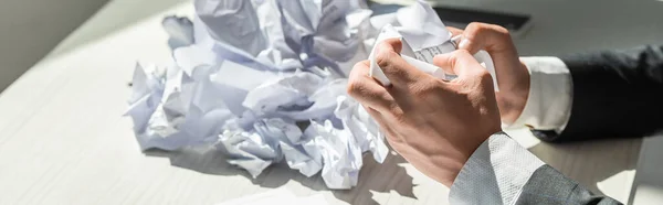 Ausgeschnittene Ansicht eines Geschäftsmannes mit Händen in der Nähe eines Stapels zerbröselter Papiere auf verschwommenem Hintergrund, Banner — Stockfoto