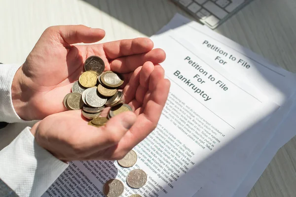 Vista recortada del empresario sosteniendo monedas cerca de peticiones de bancarrota sobre fondo texturizado blanco - foto de stock