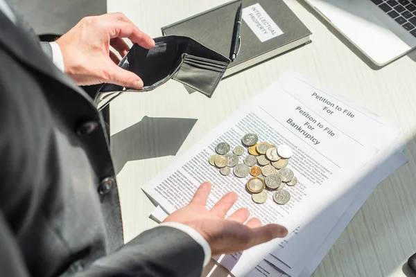 Vista recortada del empresario sosteniendo cartera vacía cerca de monedas en peticiones de bancarrota en primer plano borroso - foto de stock