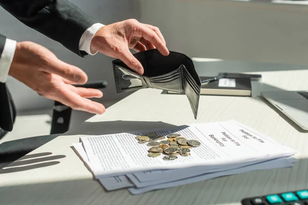 Обрезанный взгляд бизнесмена с пустым кошельком рядом с монетами на петиции о банкротстве на столе — стоковое фото