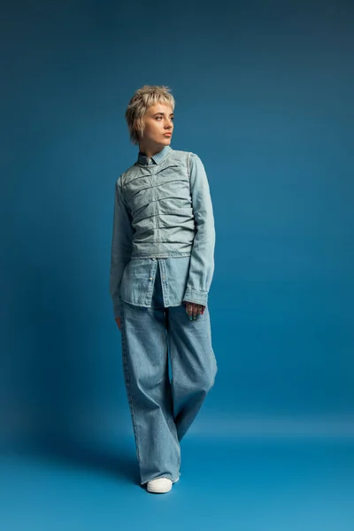 Шикарная молодая женщина в джинсах уверенно стоит на ярком синем фоне. — стоковое фото