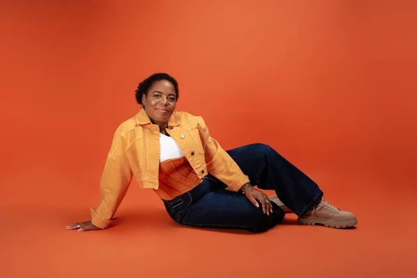 Una mujer afroamericana de tamaño grande y confiada exhibe su atuendo de moda en otoño en un vibrante estudio. - foto de stock