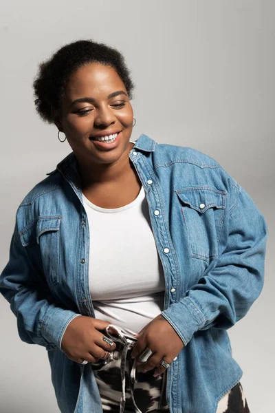 Una mujer confiada de talla grande que viste un atuendo de otoño moderno posa en un estudio, sonriendo alegremente. - foto de stock