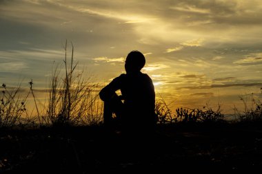 Çimen çiçek ile günbatımı gökyüzünde yalnız adam silüeti.