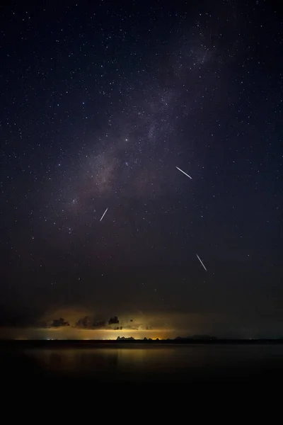 Stardust in dark night with noise and grain on the sky with shooting stars and light of city on bottom.