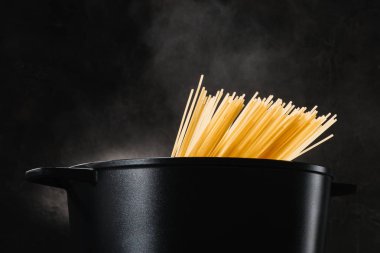 koyu arka plan üzerinde siyah tavada kaynama spagetti
