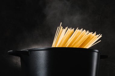 spaghetti boiling in black pan on dark background clipart