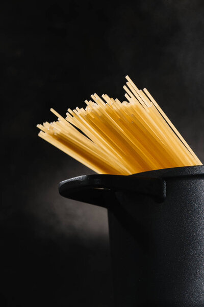 close-up shot of spaghetti boiling in black pan on dark background