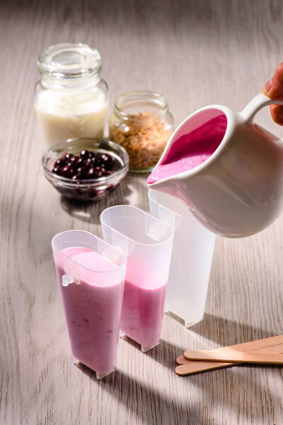 Hand poring mix in ice pops molds on wooden background