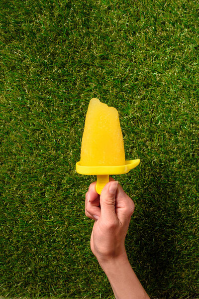 Sweet fruit Popsicle in hand on green grass background