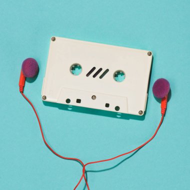flat lay with white retro audio cassette and earphones isolated on blue clipart