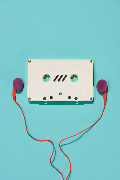 flat lay with white retro audio cassette and earphones isolated on blue
