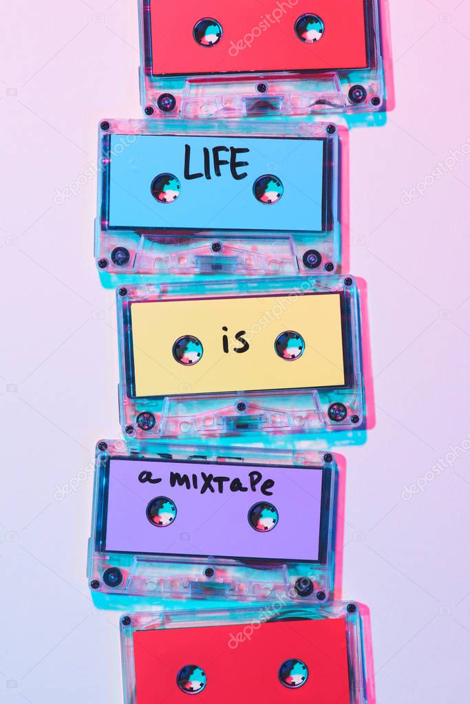 top view of arranged colorful audio cassettes with life is a mixtape inscription on purple background
