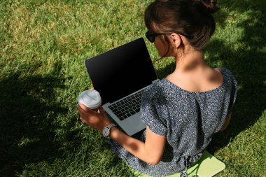 Arkadan Görünüş Freelancer kahve ile Park yeşil çim üstünde laptop üzerinde çalışmaya gitmek için