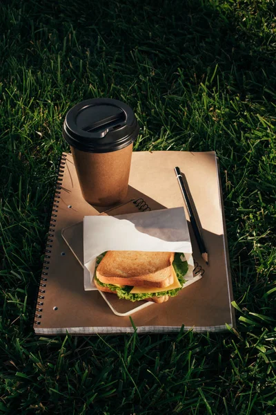 ノートブック サンドイッチとコーヒーを緑の芝生の上のクローズ アップ表示  — 無料ストックフォト