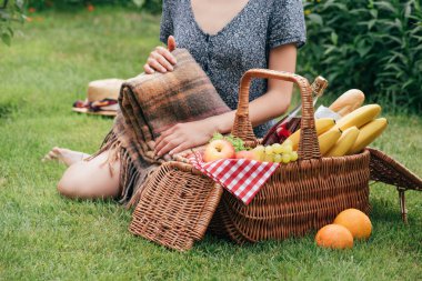 battaniye tutan ve piknik Park yeşil çimenlerin üzerinde oturan kadın kırpılmış görüntü