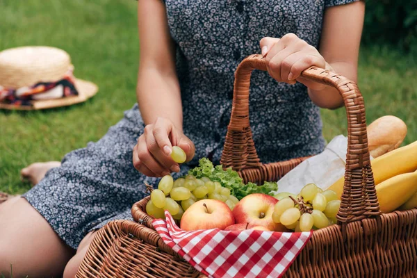 yeşil çimenlerin üzerinde oturan ve üzüm pikniğinde alarak kadın kırpılmış görüntü