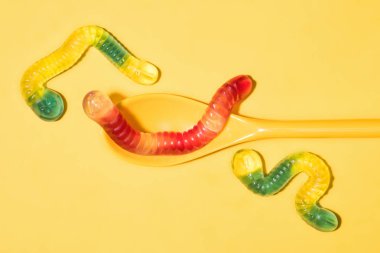 top view of delicious gummy worms with spoon on yellow clipart