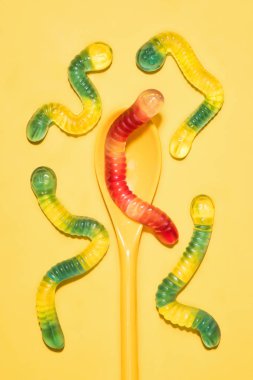 top view of colorful gummy worms with spoon on yellow clipart