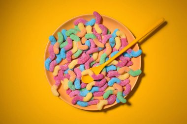top view of gummy worms with spoon on plate and on yellow clipart