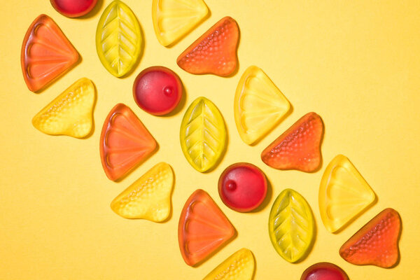top view of gummy fruits in row on yellow surface