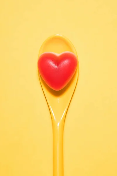 在勺子和黄色表面上的红色心脏形状的美味糖果的顶级视图 — 图库照片
