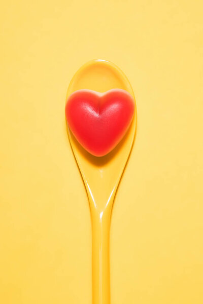 top view of delicious candy in shape of red heart on spoon and on yellow surface