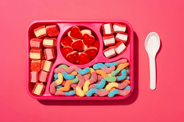 top view of gummy candies on plastic tray on pink surface