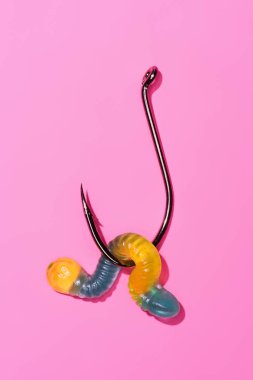 colorful gummy worm on fishing hook on pink clipart