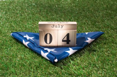 close up view of folded american flag and wooden calendar with 4th july date on green lawn, americas independence day concept clipart