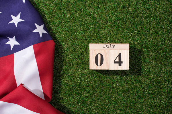 вид сверху на американский флаг и деревянный календарь с 4 июля на зеленой лужайке, концепция Дня независимости Америки
