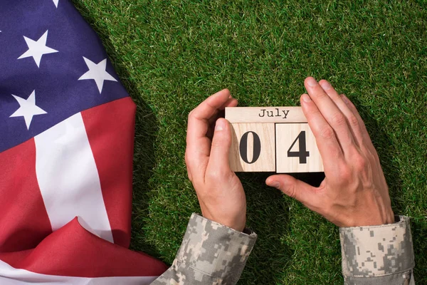 士兵在军事制服持有日历与7月4日日期与美国国旗绿草 美洲独立日概念的裁剪射击 — 图库照片
