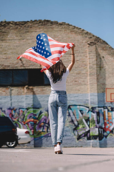 Вид сзади женщины с флагом США в руках, стоящей на улице, концепция праздника 4 июля
