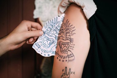 cropped shot of tattoo artist transferring tattoo sketch on shoulder in tattoo salon  clipart