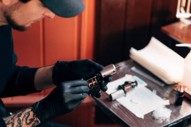selective focus of tattoo artist in gloves with tattooing machine in salon clipart