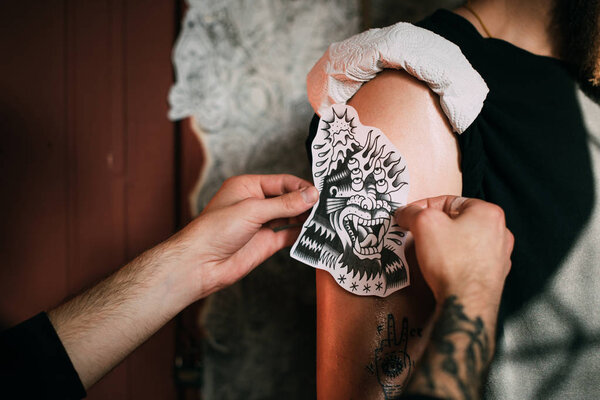 cropped shot of tattoo artist transferring tattoo sketch on shoulder in tattoo salon 