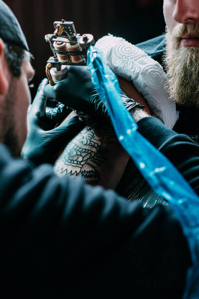 cropped shot of tattooing process of tattoo on shoulder in salon