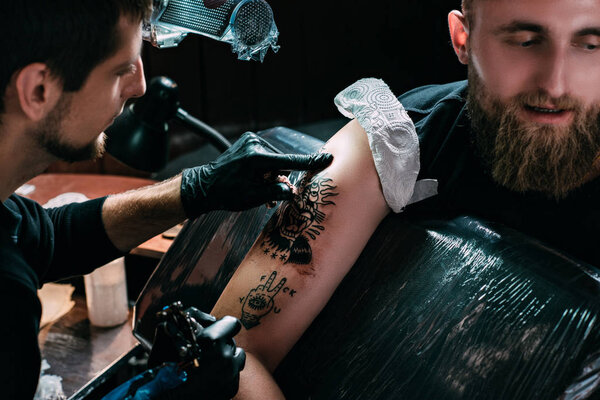 selective focus of tattoo artist in gloves working on tattoo on shoulder in salon