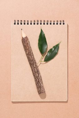 top view of wooden pencil with green leaves on blank notebook on beige clipart