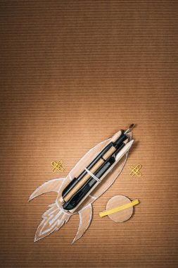 top view of handmade cardboard rocket with stationery and planet on brown background clipart