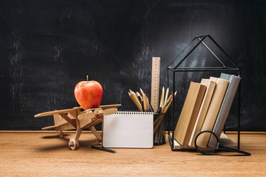 ahşap oyuncak uçak, defter, kitap ve kalem boş yazı tahtası ile masa üzerinde apple'nın görünümü kadar kapatın