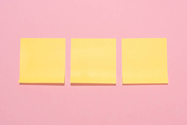 top view of blank yellow stick it notes placed in row on pink 