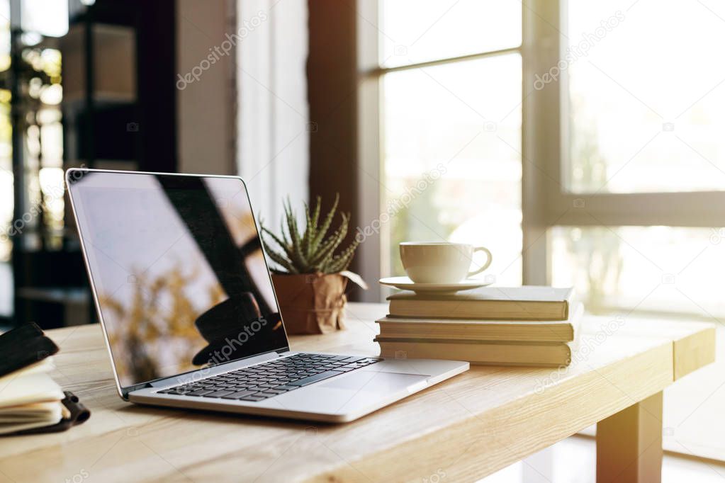 selective focus of laptop with blank screen at table with books and cup of coffee 