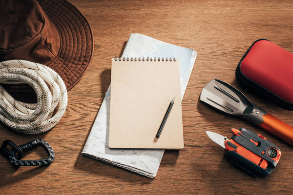 top view of blank notebook with pencil, map and travel items on wooden table