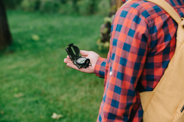 cropped shot of young man in checkered shirt holding compass in forest