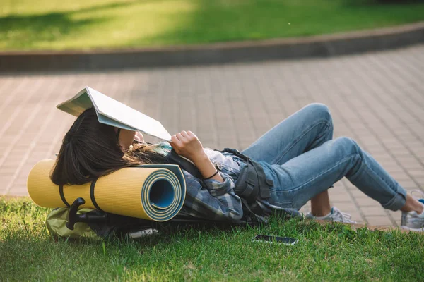 Mädchen Hält Karte Gesicht Während Sie Mit Rucksack Gras Liegt — Stockfoto